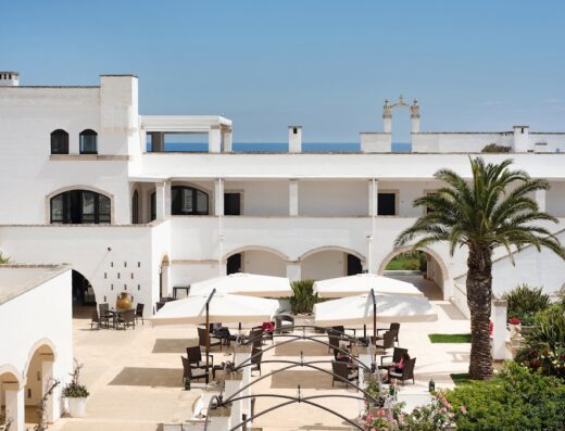 Vista aerea del Borgobianco Resort & Spa Polignano - MGallery Collection, con architettura bianca, cortile con ombrelloni e vegetazione lussureggiante.