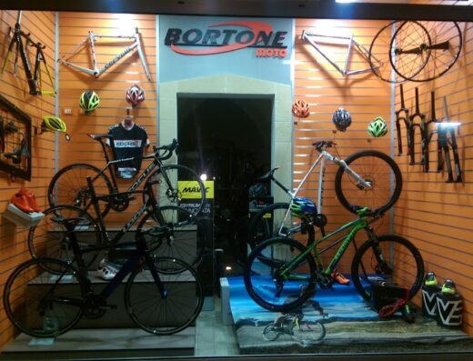Vetrina del negozio Bortonemoto SAS con esposizione di biciclette da corsa, mountain bike, telai, ruote, caschi e accessori per ciclisti. Negozio specializzato nella vendita e riparazione di biciclette.