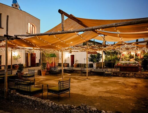 Patio esterno illuminato al Bosco De' Medici Hotel & Resort, con arredi da giardino e tettoia di legno con luci, creando un'atmosfera accogliente per i visitatori.