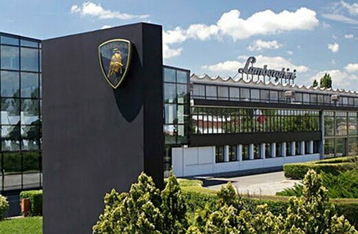 Esterno della sede Automobili Lamborghini con il logo del toro dorato. Architettura moderna con ampie vetrate e insegna "Lamborghini" sul tetto.