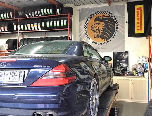 Auto AMG blu su un ponte sollevatore presso Bramante Pneumatici, con scaffali di pneumatici e banner Pirelli sullo sfondo.