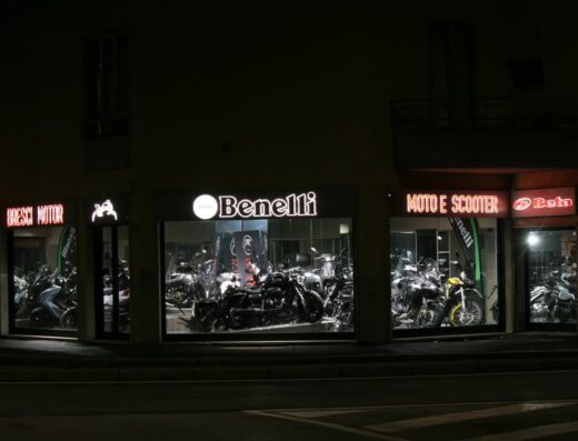 Concessionario Bresci Motor di notte con vetrine illuminate che espongono moto Benelli e Beta, vendita moto e scooter