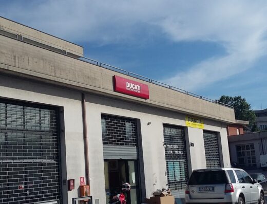 Brothers Moto: una concessionaria Ducati Service con moto parcheggiata di fronte e un SUV in sosta, cielo azzurro sullo sfondo. Servizi di riparazione e vendita accessori moto.