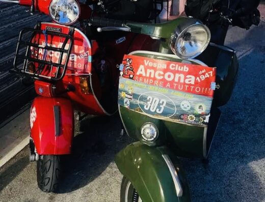 Due scooter Vespa, uno rosso con portapacchi anteriore e uno verde con adesivo del Vespa Club Ancona, parcheggiati uno accanto all'altro.