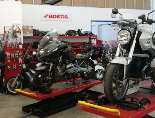 Officina C.m. Motori S.n.c.: Motociclette Honda e BMW su piattaforme elevatrici per manutenzione e riparazione. Accessori moto visibili sullo sfondo.