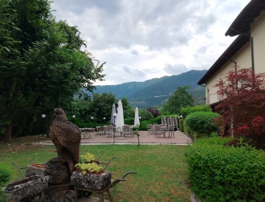 Immagine di Ca' del Bosco che mostra un giardino verde con una scultura di aquila in legno, tavoli all'aperto e montagne sullo sfondo.