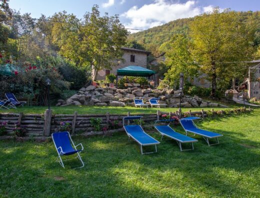 Cà Gabrielli Agriturismo: Veduta del curato giardino con sedie a sdraio blu, rocce decorative e vegetazione lussureggiante, ideale per relax e vacanza.