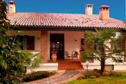 Cà Livenza Sacile B&B exterior view featuring a charming Italian villa with a tiled roof, palm trees, and outdoor seating, perfect for a relaxing stay in Sacile. Explore local destinations and enjoy the amenities of this inviting bed and breakfast.