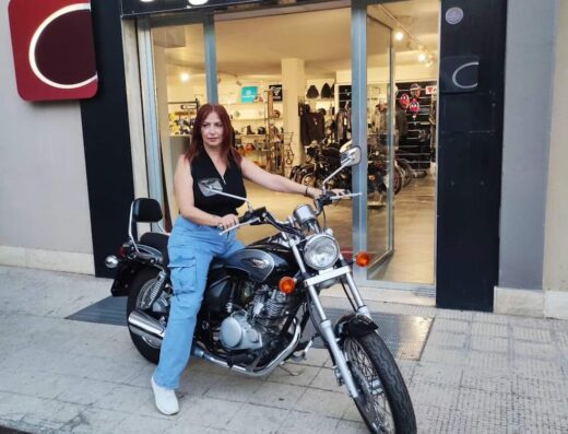 Una donna su una moto di fronte al negozio Cagnazzi Moto, che vende accessori e offre servizi per motociclisti dal 1945.