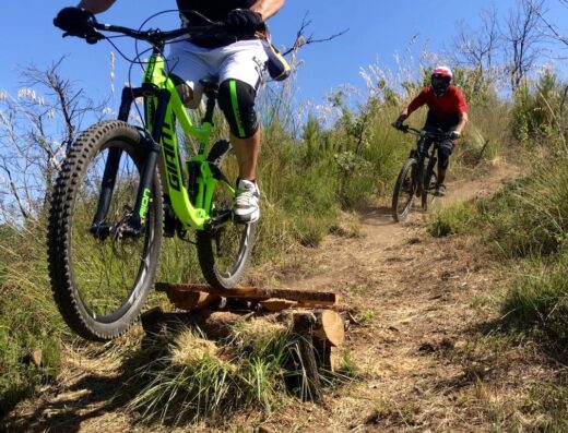 Ciclista professionista con mountain bike Giant verde brillante esegue un salto acrobatico su percorso sterrato in Calabria Bike Resort Srl, accessori e casco protettivo.