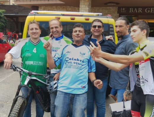 Gruppo di ciclisti e appassionati di moto Calabrò Cici Moto posano per un selfie davanti a un furgone e un negozio, promuovendo il negozio di moto Calabrò a Pellaro, Reggio Calabria.