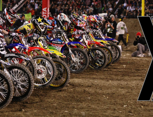 Una fila di motociclisti di motocross pronti alla partenza, con moto da competizione allineate e folla sullo sfondo, ideale per elaborazioni e accessori moto.