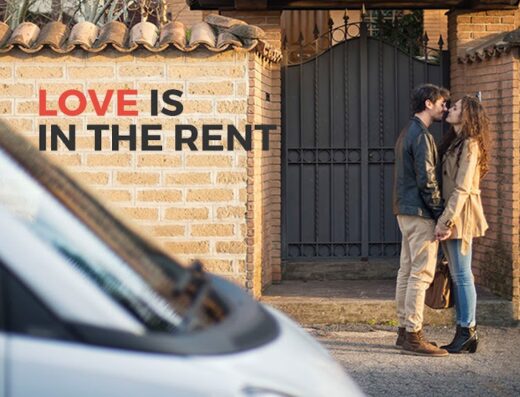 A young couple kisses in front of a brick wall with the words "Love is in the rent" superimposed, and a white car is partially visible.