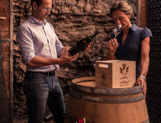 Cantina Al Rocol: Un uomo esamina una bottiglia di vino mentre una donna ne assapora l'aroma in una cantina rustica con botti.