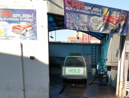 Car Splash Autolavaggio a Mano: Vista dell'autolavaggio con furgone in attesa del lavaggio accurato. Insegne con informazioni e numeri di telefono visibili.