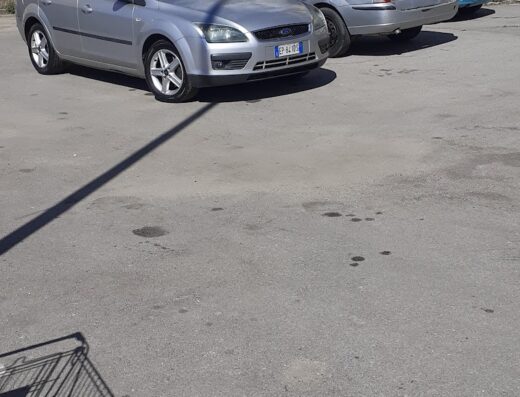 Auto grigia parcheggiata in un'area di lavaggio auto, con edificio sullo sfondo. Servizi professionali per la cura e la pulizia della tua auto.