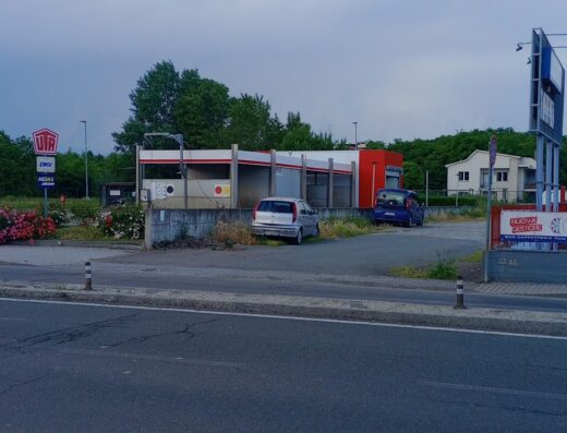 Autolavaggio self-service con due auto parcheggiate, una grigia e una blu, in una giornata nuvolosa. Servizi per auto e moto.