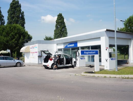 Un uomo pulisce l'interno di un'auto bianca presso un autolavaggio a Marcon, con aspirapolveri in evidenza e un'altra auto parcheggiata nelle vicinanze.