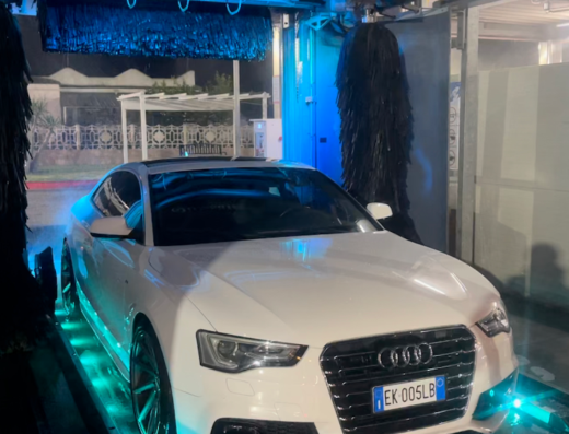 Auto bianca in un autolavaggio a Tre Fontane, Roma, durante il lavaggio con spazzole e illuminazione blu. Servizio di pulizia auto.