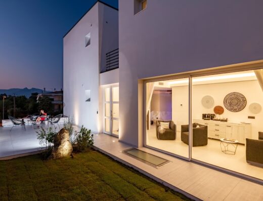 Exterior view of Cara a Bentu charming rooms featuring a modern white building, outdoor seating area with guests, and a glimpse of the interior design.