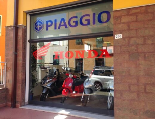 Concessionaria moto con vetrina che espone marchi Piaggio e Honda, con scooter visibili all'interno. Servizi di vendita e assistenza per moto e accessori.