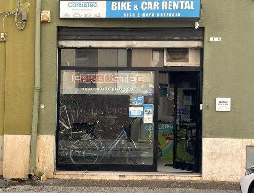 Foto della facciata di CarBusTec a Stazione Centrale, negozio di noleggio scooter, biciclette, auto e moto. Insegna con logo CarBusTec e scritta 'Bike & Car Rental', vetrina con biciclette visibili.