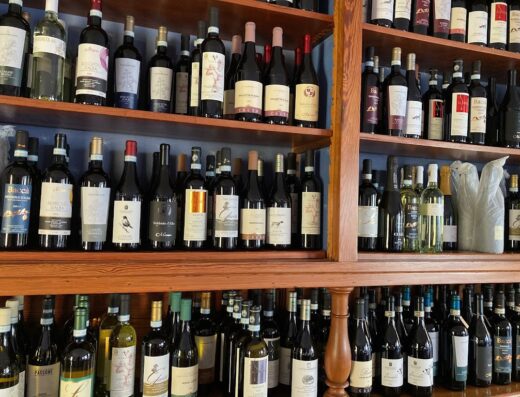 Scaffalature di legno piene di bottiglie di vino rosso e bianco a Casa Barbabuc, con etichette visibili.
