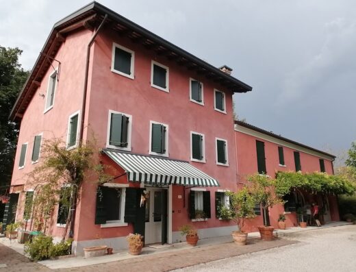 Casa Carrer B&B: Esterno di un edificio rosa a due piani con finestre verdi e tenda a righe sopra l'ingresso, circondato da piante.