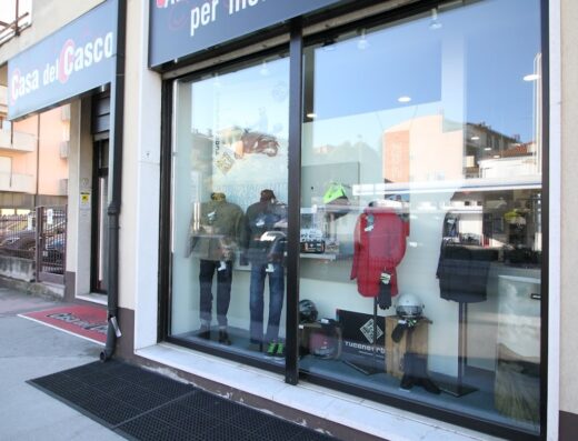 Vetrina del negozio Casa del Casco con abbigliamento e accessori per moto e scooter in esposizione, caschi, giacche e pantaloni da motociclista.