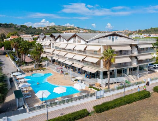 Aerial view of Casa del Mar Residence & Beach Resort, featuring a pool with umbrellas, beachfront access, and views of the surrounding landscape.
