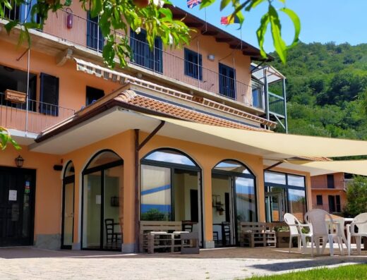Vista esterna dell'Hotel Casa Didé, con terrazza coperta, tavoli e sedie per ristorazione all'aperto in un ambiente rilassante.