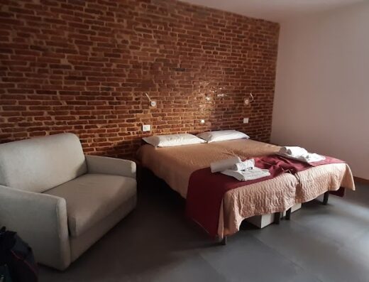 Camera accogliente a Casa Orrù con letto matrimoniale, divano e parete in mattoni a vista. Arredamento confortevole per un soggiorno rilassante.