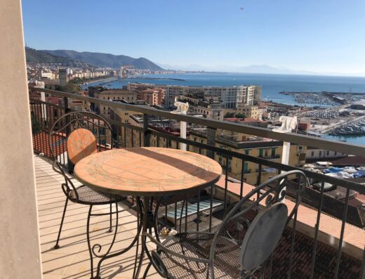 Terrazza panoramica con tavolo e sedie in ferro battuto affacciata sul mare di Salerno, in Campania, Italia. Vista sulla città e sul porto.
