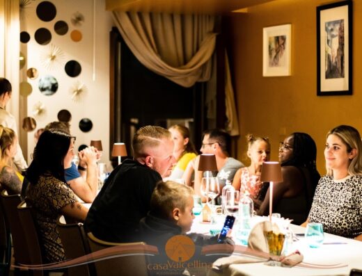 Persone sedute a un tavolo in un ristorante di Casa Valcellina, con bicchieri di vino, lampade da tavolo e decorazioni artistiche alle pareti.