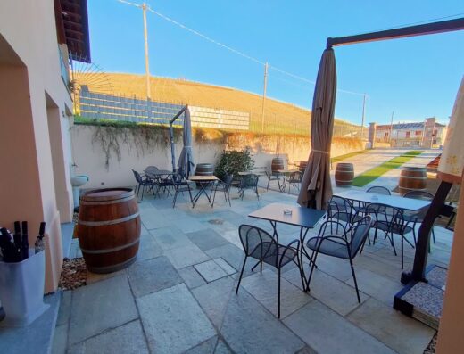 Cascina Bellonuovo: vista esterna dell'area ristoro con tavoli, sedie, ombrelloni e botti di legno decorative, ideale per una pausa durante un viaggio in moto