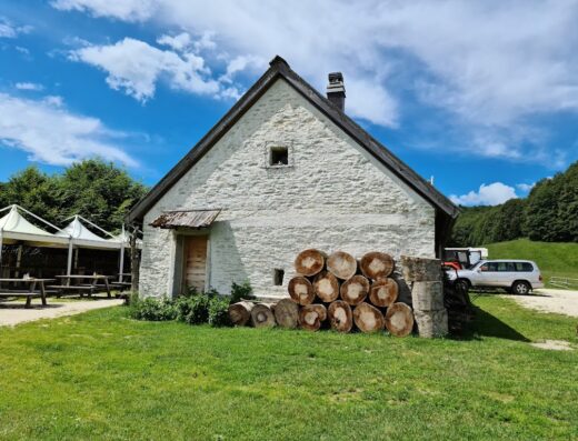 Casera Le Rotte: Rustico edificio in pietra con legna accatastata, auto parcheggiata e tavoli esterni in un paesaggio montano.