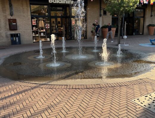 Fontana decorativa di fronte al negozio Baldinini a Castel Guelfo The Style Outlets, con bandiere colorate e pavimentazione in mattoni
