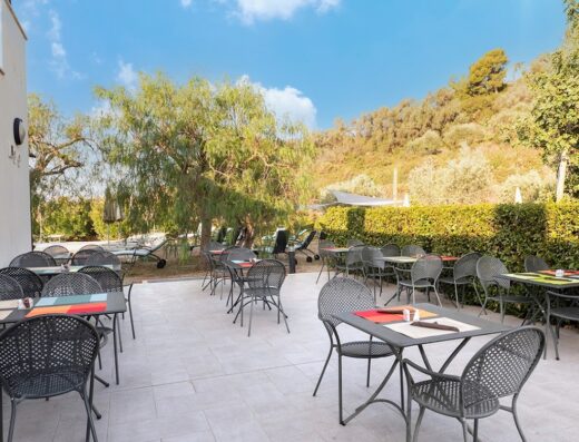Ristorante all'aperto del Castellaro Golf Resort Hotel con tavoli e sedie in metallo su una terrazza soleggiata.