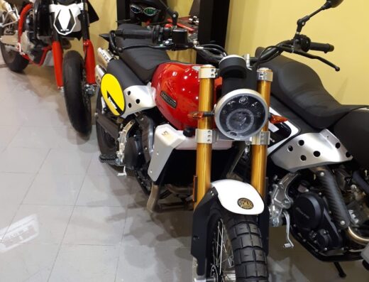 Catamoto di Catalano Marco: Lineup of Caballero motorcycles, including a red Scrambler model with knobby tires, plus helmets on display.