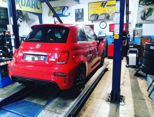 Auto rossa Abarth 595 su ponte sollevatore presso Caviola Gomme, officina specializzata in pneumatici e servizi per auto e moto.