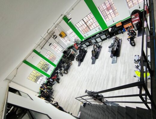 Vista dall'alto di un garage per moto con diverse motociclette esposte, attrezzi e accessori per la riparazione e la manutenzione.