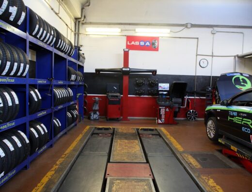 Interno di un'officina a Cecina con scaffali di pneumatici Goodyear, attrezzatura per revisioni e collaudi auto, e un'auto sul ponte elevatore. Servizi di manutenzione e riparazione veicoli.