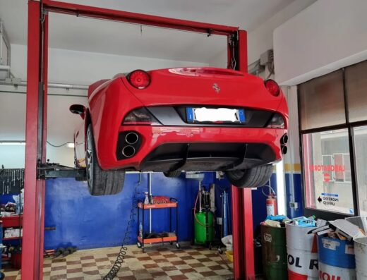 Ferrari rossa sollevata su un ponte elevatore in un'officina di Cento Motor Service per manutenzione e riparazione auto di lusso.