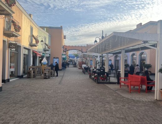 Centro commerciale Atec Group con negozi, tavoli all'aperto e cielo nuvoloso, ideale per lo shopping e il tempo libero