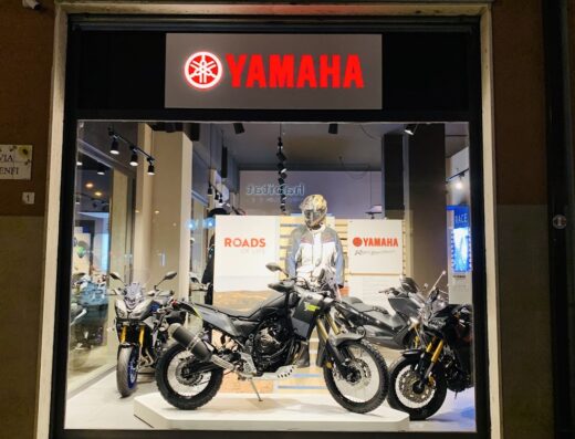Vetrina di Centro Moto Yamaha SRLS con esposizione di moto Yamaha, accessori e abbigliamento da motociclista. Scooter e moto da viaggio visibili.
