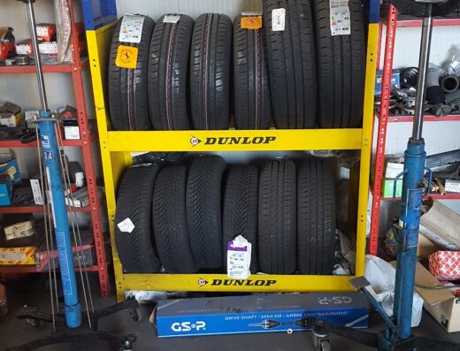 Scaffale di pneumatici nuovi Goodyear e Dunlop in un'officina meccanica gommista, con attrezzature per il cambio gomme visibili.