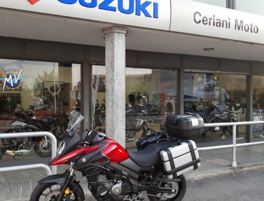 Una moto Suzuki V-Strom rossa e nera parcheggiata di fronte al negozio Ceriani Moto, concessionario di moto e accessori per motociclisti
