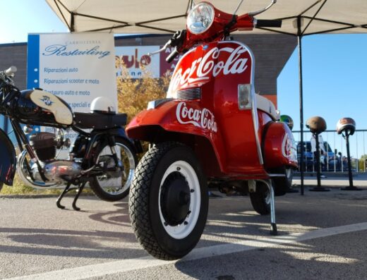 Cervignano Motor Festival: Vespa d'epoca rossa personalizzata Coca-Cola e moto d'epoca esposte, accessori moto, riparazioni scooter e moto.