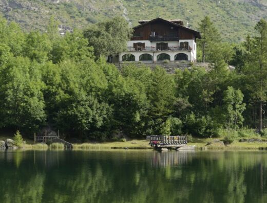 Chalet sul Lago Hotel a Moncenisio, Piemonte: Immagine del lago con riflessi, circondato da alberi e con l'hotel in collina sullo sfondo.