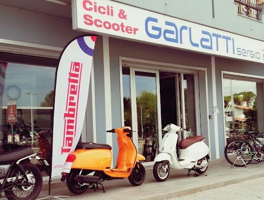 Showcase di Cicli e Scooter Garlatti Sergio con moto custom, scooter Lambretta arancione e bianco, e biciclette esposte.